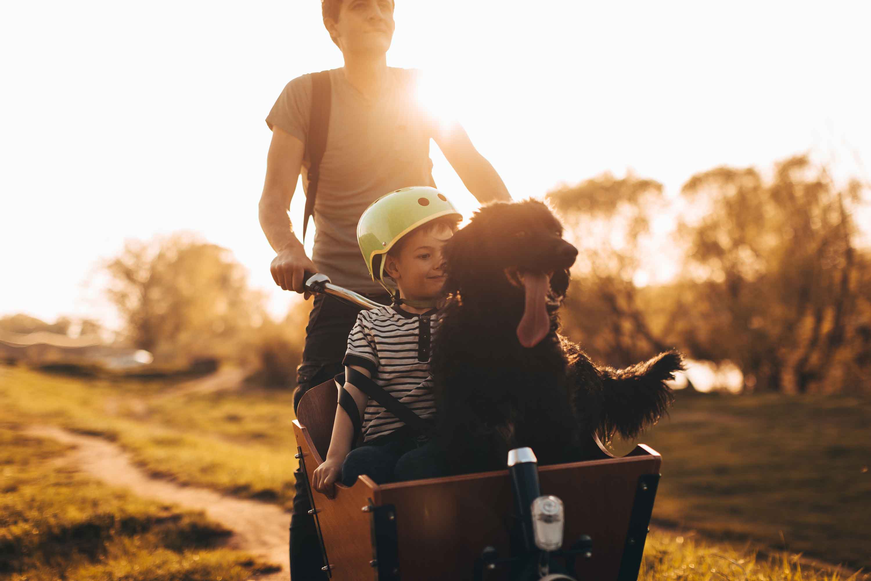 man riding a cargo bike in front sits a child with his dog - Flamingo Pet Products