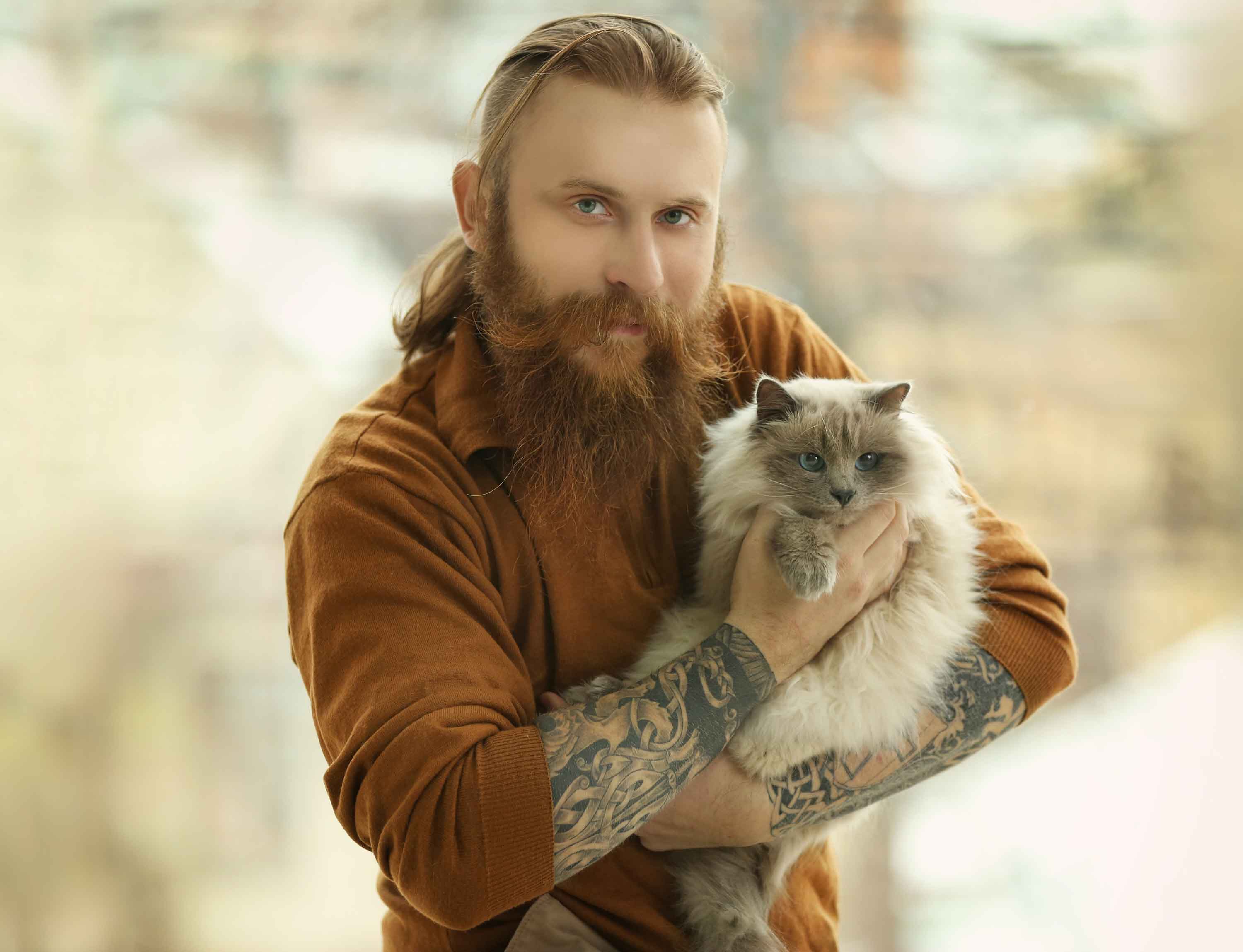 A tattooed man with a long beard poses with a cat - Flamingo Pet Products